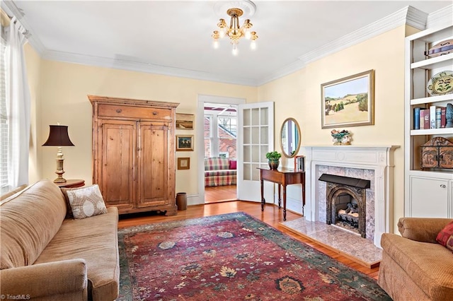 living room featuring built in shelves, ornamental molding, wood finished floors, an inviting chandelier, and a fireplace