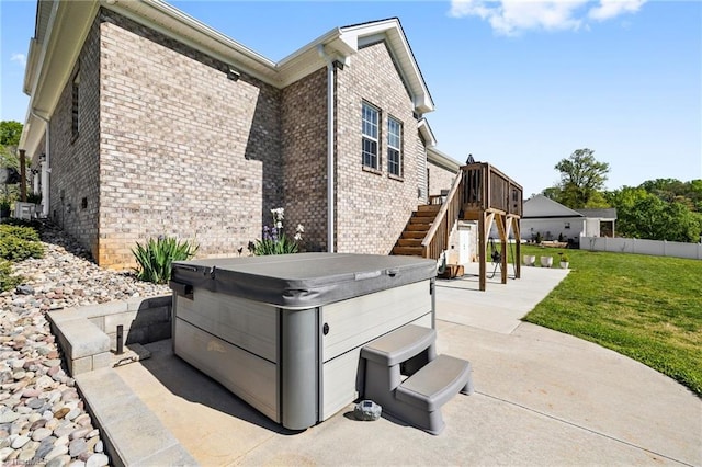 view of side of property featuring stairs, a yard, a patio area, brick siding, and a hot tub