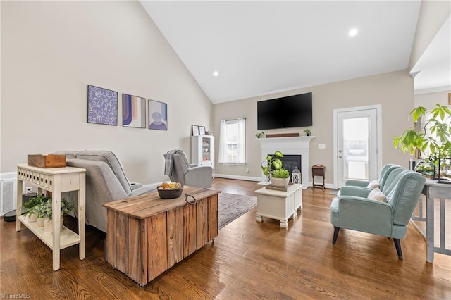 living area with a glass covered fireplace, wood finished floors, high vaulted ceiling, and recessed lighting