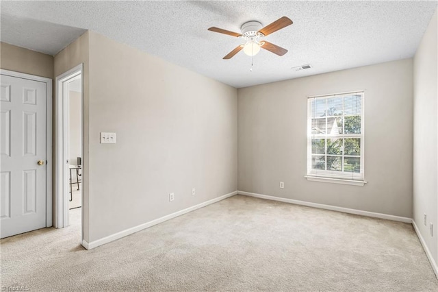 empty room featuring ceiling fan, light colored carpet, and a textured ceiling