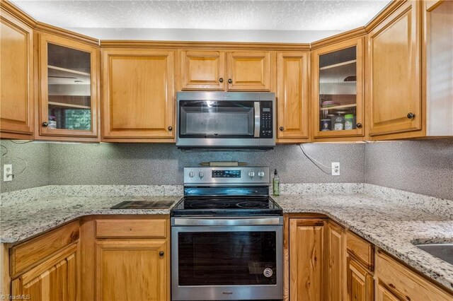 kitchen with appliances with stainless steel finishes, light stone counters, backsplash, and a textured ceiling