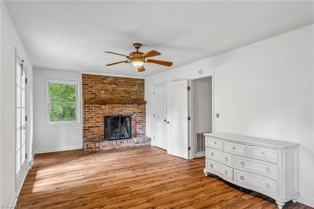 unfurnished living room featuring ceiling fan, light hardwood / wood-style flooring, brick wall, and a fireplace