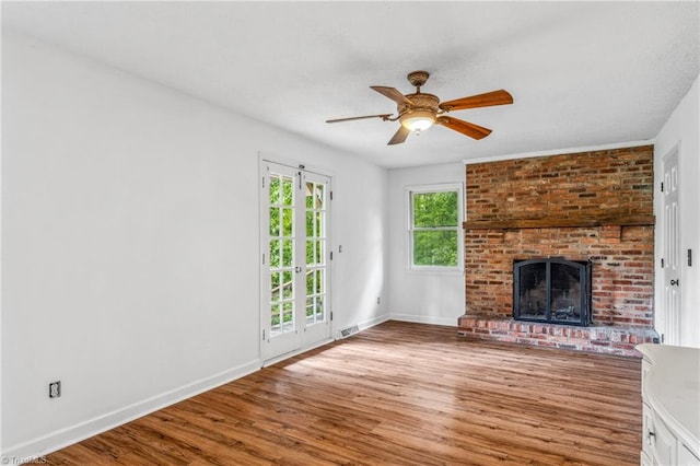 unfurnished living room featuring light hardwood / wood-style flooring, ceiling fan, brick wall, and a brick fireplace