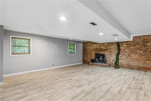 unfurnished living room with a brick fireplace, light hardwood / wood-style flooring, and brick wall