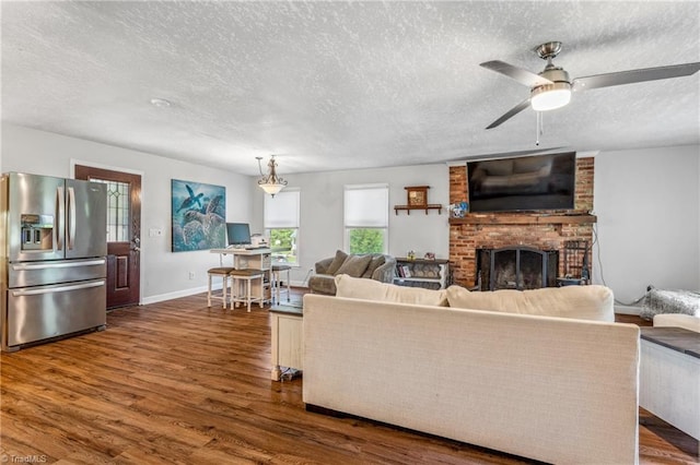 living room with brick wall, a fireplace, a textured ceiling, dark hardwood / wood-style flooring, and ceiling fan