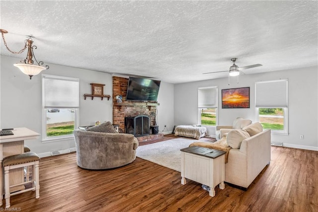 living room with ceiling fan, brick wall, a brick fireplace, hardwood / wood-style floors, and a textured ceiling