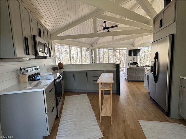 kitchen with gray cabinetry, stainless steel appliances, vaulted ceiling with beams, ceiling fan, and light hardwood / wood-style flooring