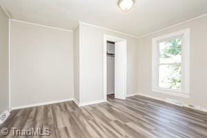 unfurnished bedroom with wood-type flooring, a closet, and crown molding