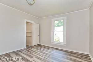 unfurnished bedroom with wood-type flooring, a walk in closet, a closet, and ornamental molding