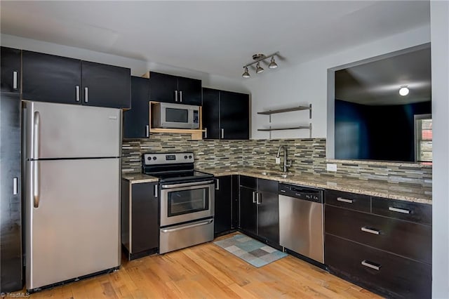 kitchen featuring light wood-style flooring, a sink, dark cabinetry, and appliances with stainless steel finishes