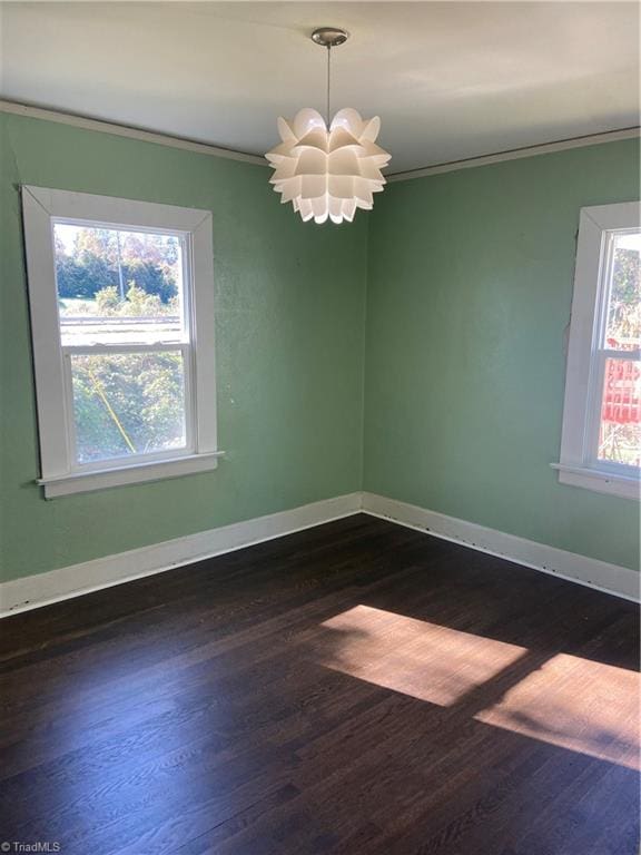 empty room featuring dark hardwood / wood-style flooring, a chandelier, and ornamental molding