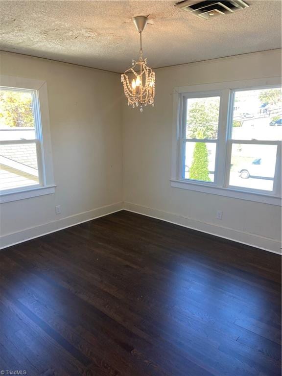 spare room featuring a chandelier, a wealth of natural light, dark wood-type flooring, and a textured ceiling