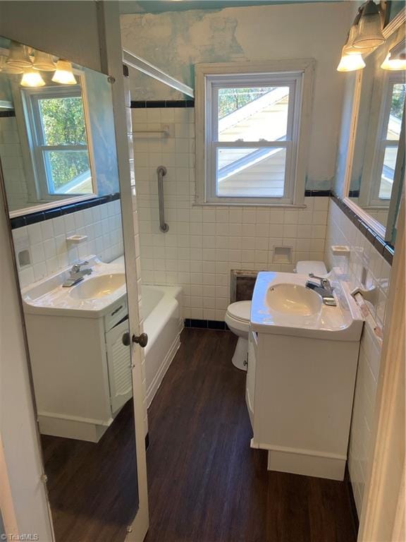 full bathroom featuring tiled shower / bath combo, wood-type flooring, toilet, vanity, and tile walls