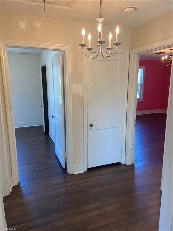 corridor with a textured ceiling, a notable chandelier, and dark wood-type flooring