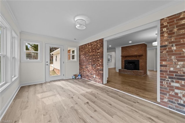 unfurnished living room with ornamental molding, wood finished floors, brick wall, baseboards, and a brick fireplace