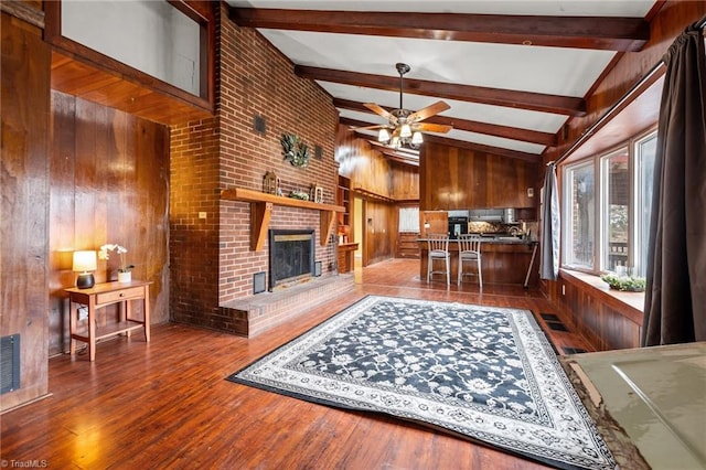 living room with wooden walls, ceiling fan, a fireplace, beamed ceiling, and wood-type flooring