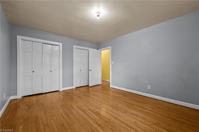 unfurnished bedroom featuring light hardwood / wood-style floors and multiple closets