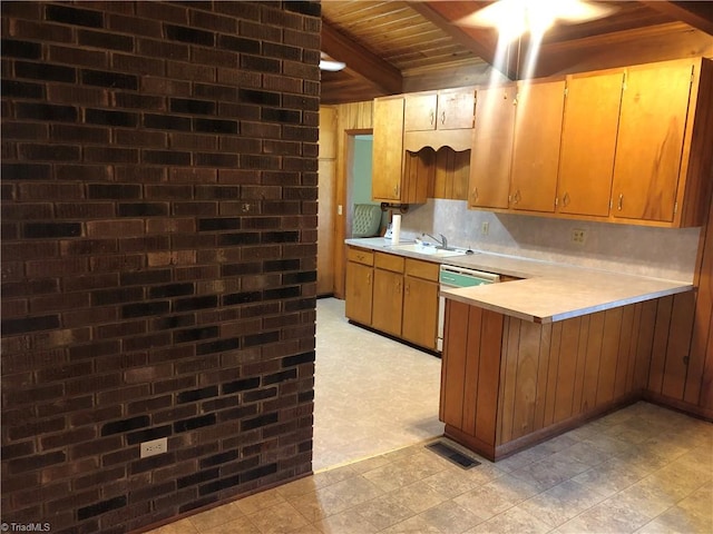 kitchen featuring beamed ceiling, white dishwasher, sink, kitchen peninsula, and brick wall