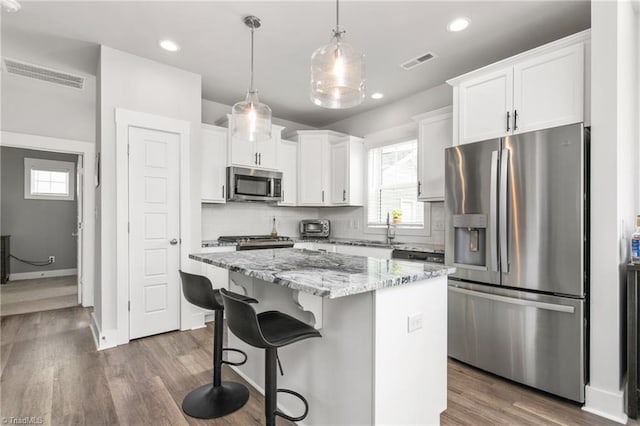 kitchen featuring stainless steel appliances, a center island, a wealth of natural light, white cabinets, and decorative light fixtures