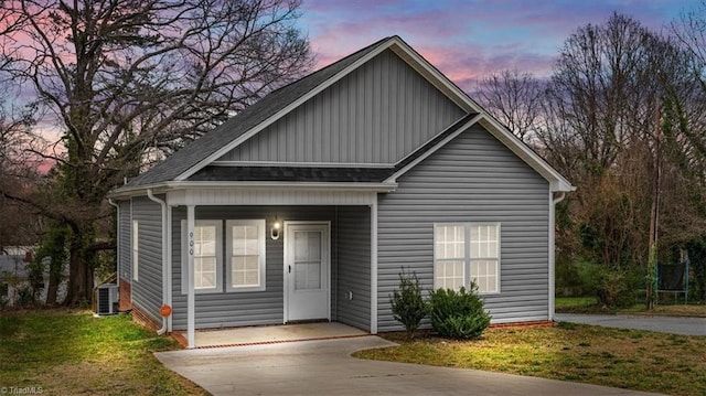 bungalow-style house with central AC, board and batten siding, concrete driveway, a front yard, and roof with shingles