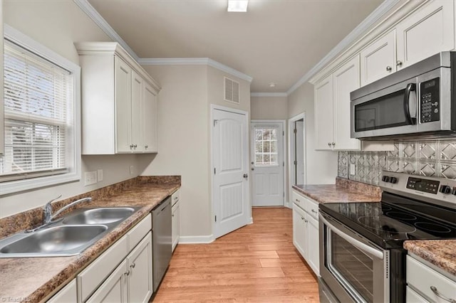 kitchen featuring visible vents, light wood-style flooring, a sink, ornamental molding, and stainless steel appliances