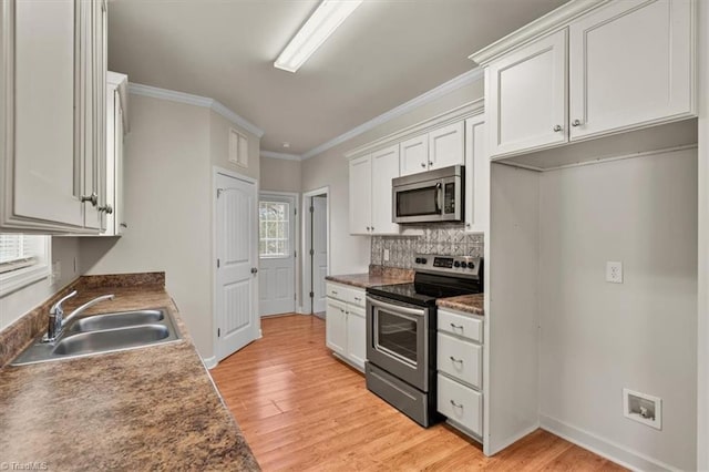 kitchen with light wood finished floors, a sink, decorative backsplash, stainless steel appliances, and white cabinets