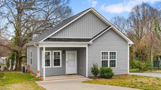 bungalow-style home with board and batten siding, a shingled roof, a trampoline, a front yard, and driveway