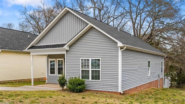 view of side of property with a lawn, board and batten siding, roof with shingles, and a patio area