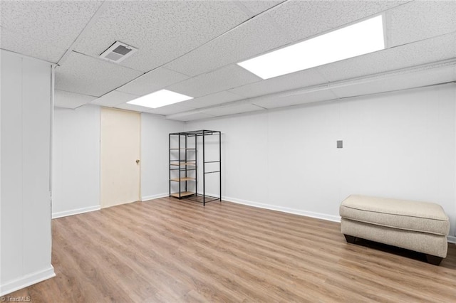 finished below grade area with wood finished floors, visible vents, a drop ceiling, and baseboards