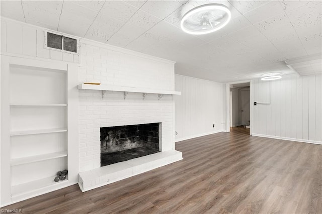 unfurnished living room with visible vents, a brick fireplace, built in shelves, and wood finished floors