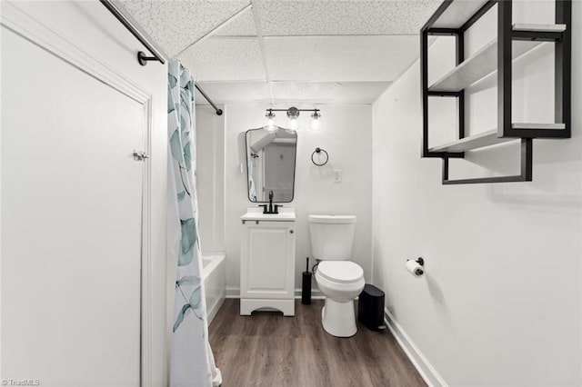 full bathroom featuring wood finished floors, baseboards, a drop ceiling, shower / bath combination with curtain, and toilet