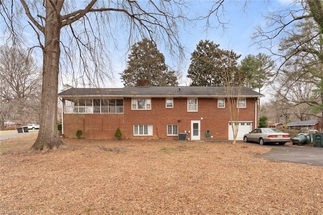 back of property with a chimney, brick siding, an attached garage, and driveway