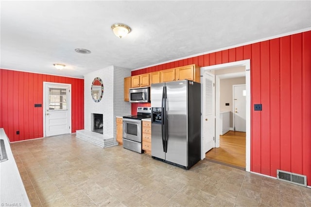 kitchen with a fireplace, visible vents, wood walls, and stainless steel appliances