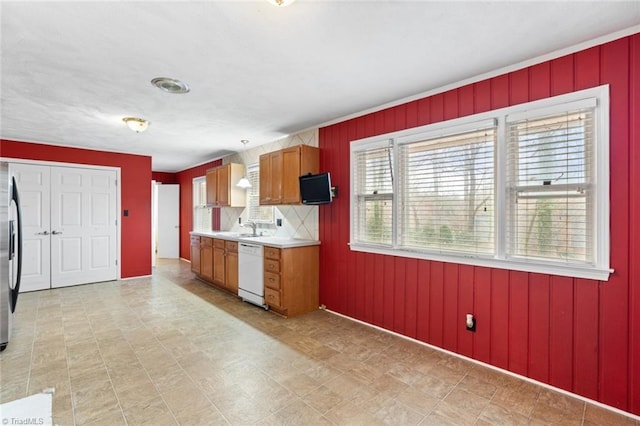 kitchen featuring white dishwasher, a sink, decorative backsplash, light countertops, and brown cabinets