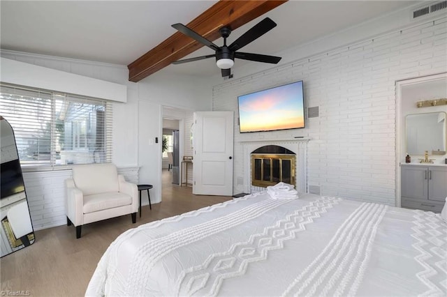 bedroom featuring beamed ceiling, hardwood / wood-style flooring, ceiling fan, and brick wall