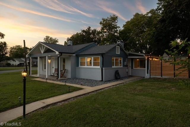 back house at dusk with covered porch and a lawn