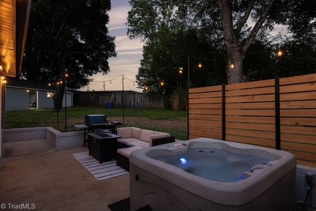 patio terrace at dusk featuring outdoor lounge area, a yard, and a hot tub