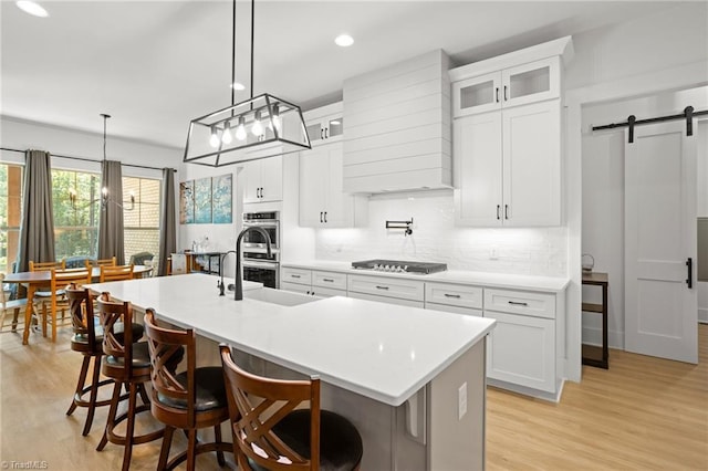 kitchen featuring stainless steel appliances, a barn door, a kitchen island with sink, and white cabinets