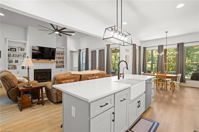 kitchen with sink, light hardwood / wood-style flooring, white cabinets, a center island with sink, and decorative light fixtures