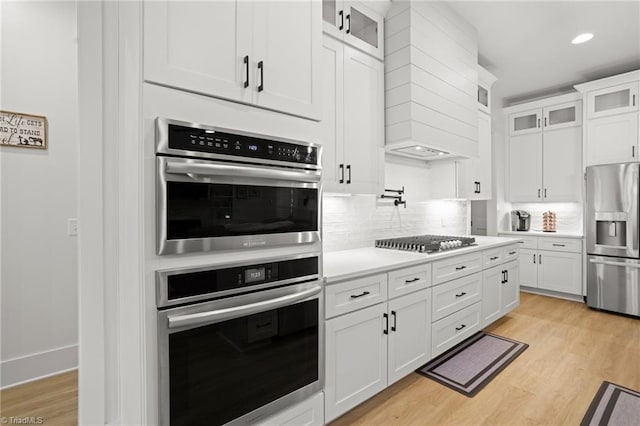 kitchen featuring white cabinetry, light wood-type flooring, tasteful backsplash, and appliances with stainless steel finishes