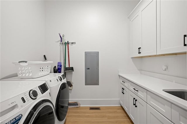 laundry area featuring light hardwood / wood-style floors, independent washer and dryer, electric panel, and cabinets