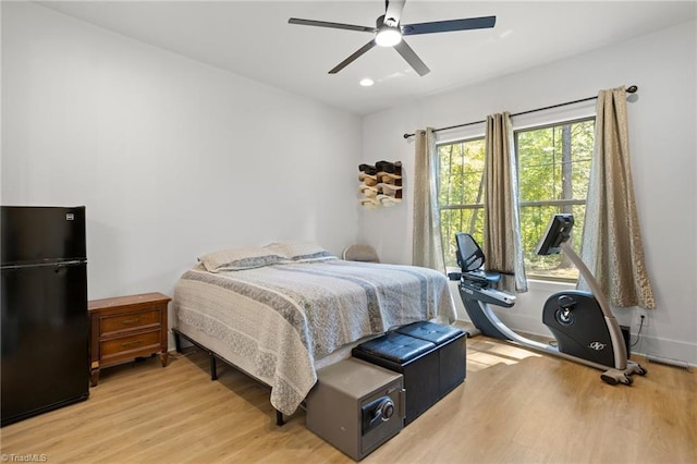 bedroom featuring light wood-type flooring, ceiling fan, and black fridge