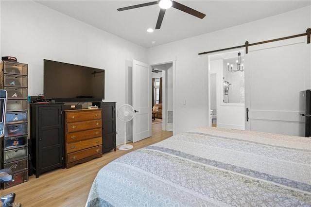 bedroom with ceiling fan, a barn door, refrigerator, and light hardwood / wood-style flooring