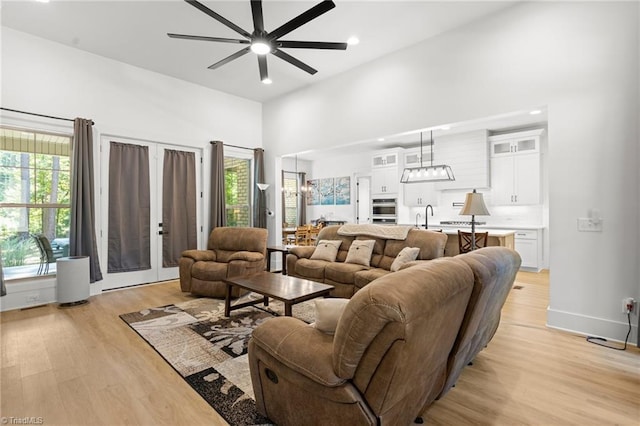 living room with ceiling fan, sink, light wood-type flooring, and a towering ceiling