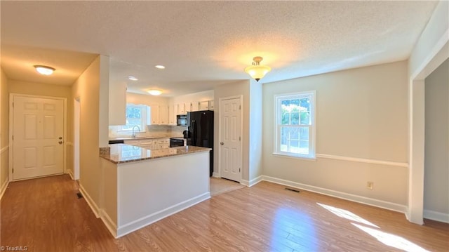 3128 Burke Mill Ct, Winston-Salem, NC 27103 - kitchen with light wood-style floors, a textured ceiling, a peninsula, black appliances, and light stone countertops