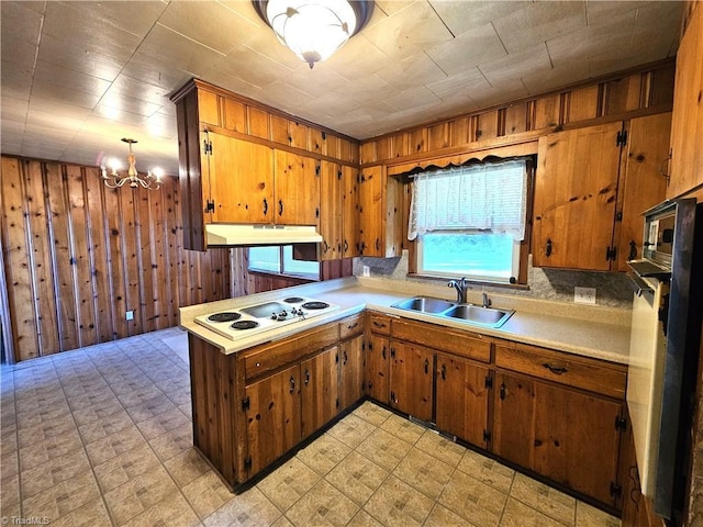 kitchen featuring sink, wood walls, a chandelier, hanging light fixtures, and white electric stovetop