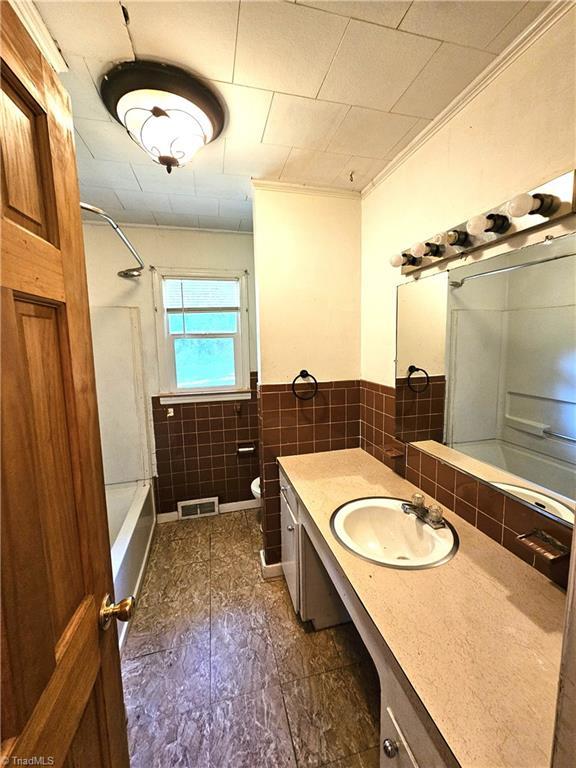 full bathroom with ornamental molding, vanity, shower / bathing tub combination, tile walls, and toilet