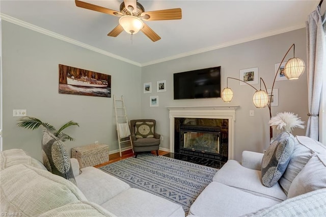 living area with wood finished floors, crown molding, a premium fireplace, ceiling fan, and baseboards