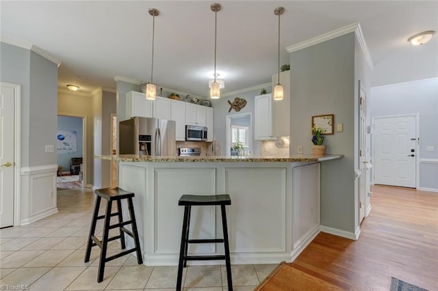 kitchen featuring appliances with stainless steel finishes, light stone countertops, white cabinets, crown molding, and a peninsula