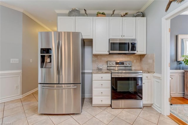kitchen with appliances with stainless steel finishes, white cabinets, light tile patterned flooring, tasteful backsplash, and ornamental molding